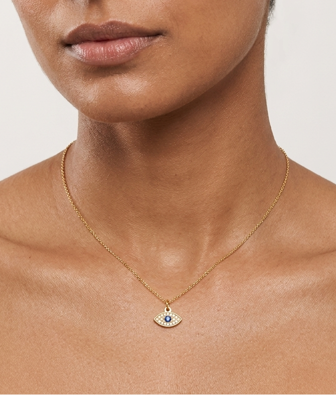 Woman wearing a gold necklace with an eye pendant on a plain background