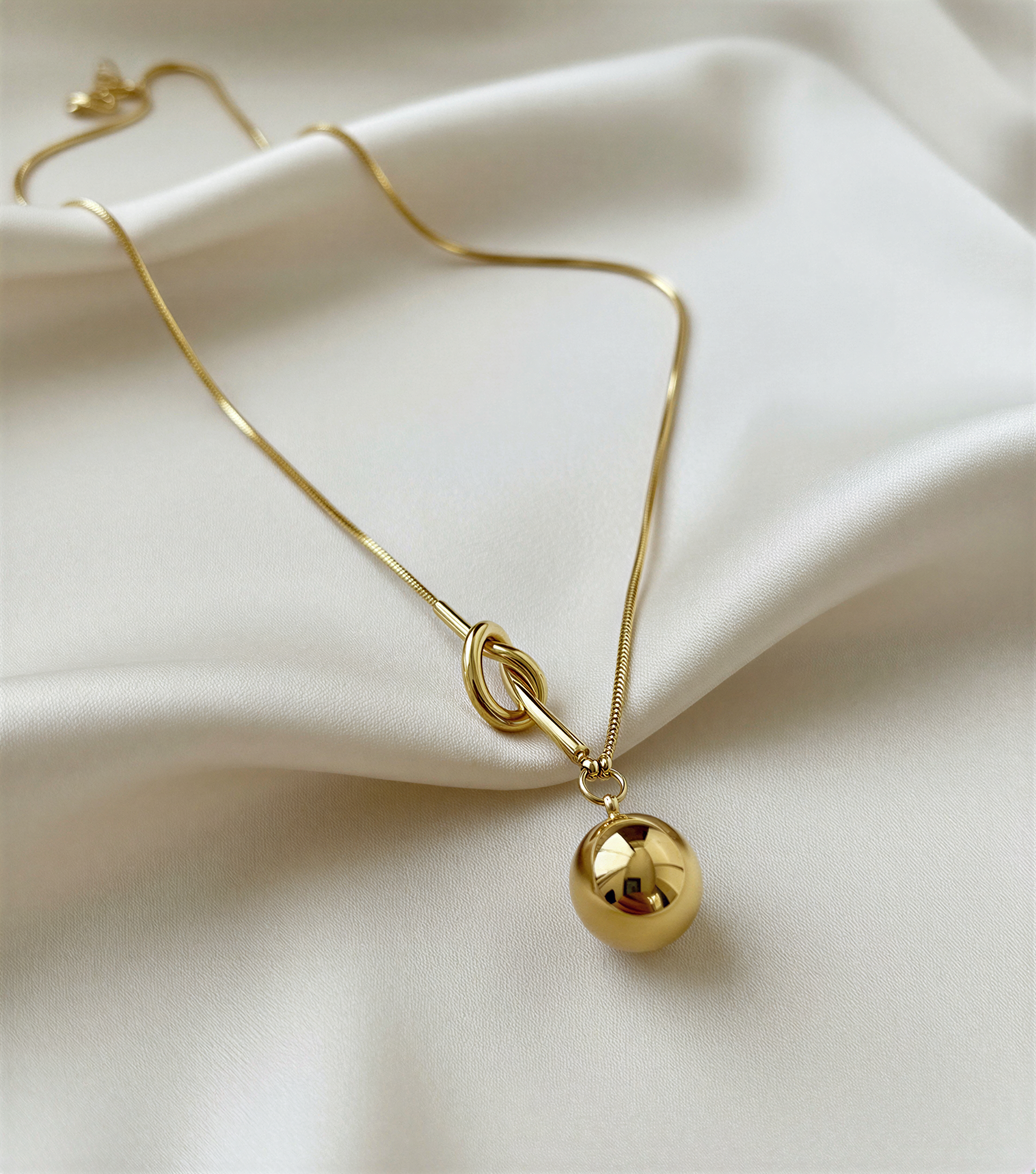 Gold necklace with a spherical pendant on a beige fabric background