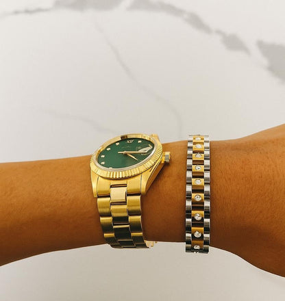 Gold watch with a green face on a wrist against a white background