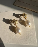 Gold star earrings with pearl drops on a textured surface