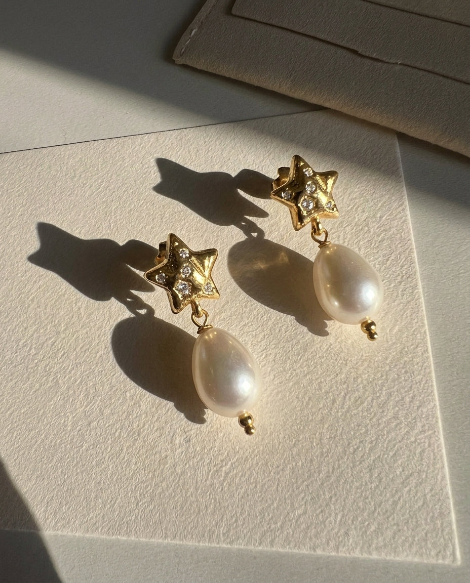 Gold star earrings with pearl drops on a textured surface