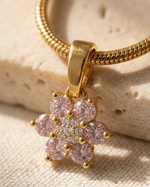 Gold necklace with a pink floral pendant on a textured beige surface