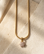 Gold necklace with a pink flower pendant on a beige fabric background
