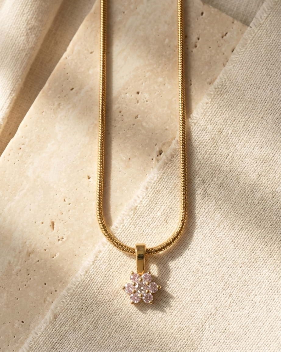 Gold necklace with a pink flower pendant on a beige fabric background