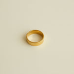 Gold ring on a light gray surface with a beige border
