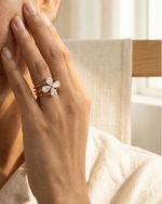 Woman wearing a gold ring with a diamond on her finger, touching her face.