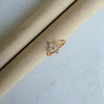 Gold ring with a diamond on a beige cushion against a light gray background
