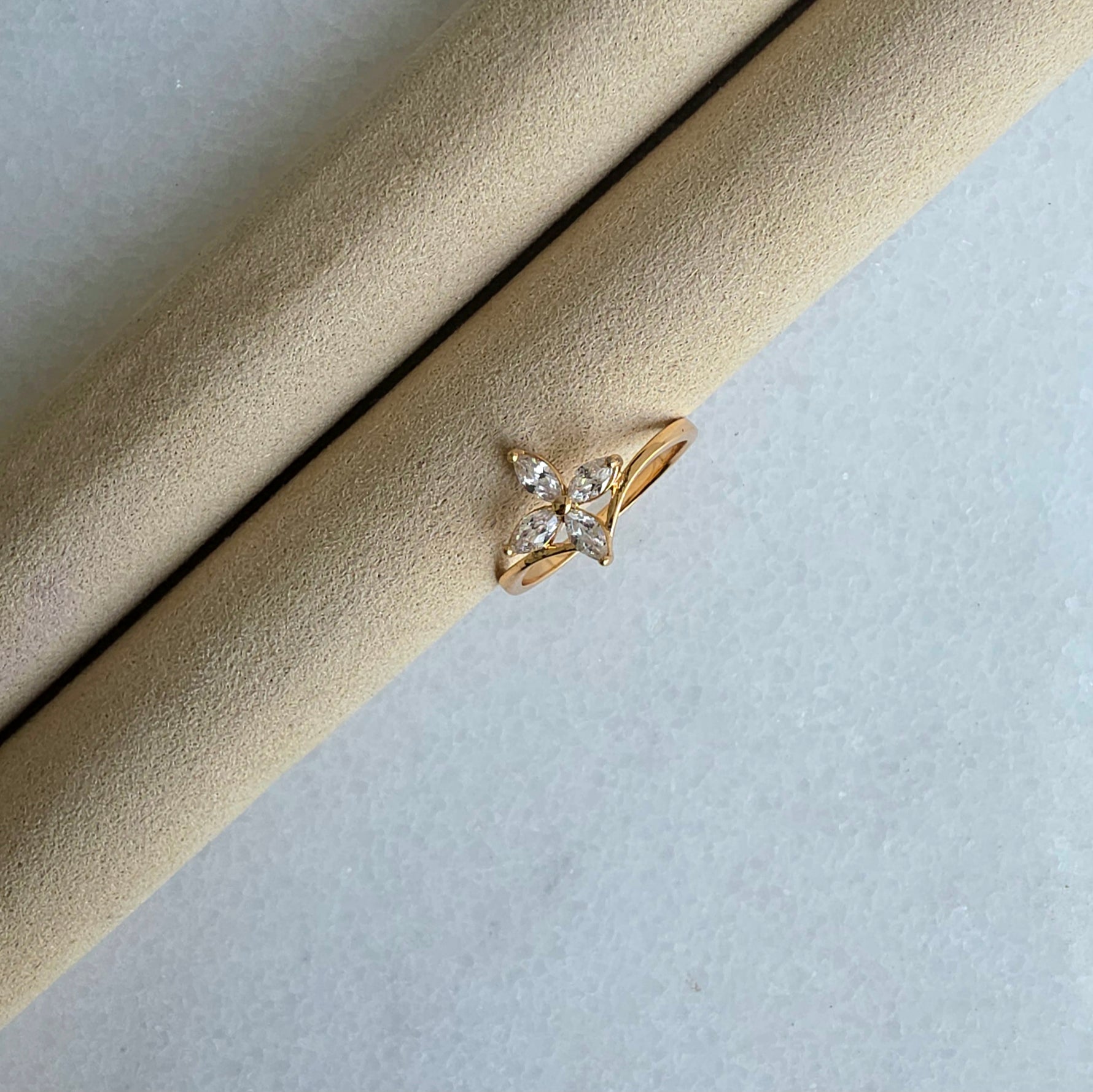 Gold ring with a diamond on a beige cushion against a light gray background