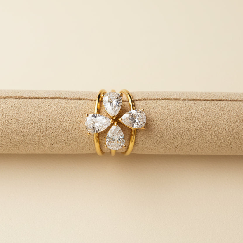 Gold ring with three clear gemstones on a beige cushion against a light gray background