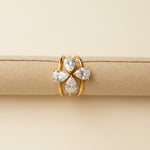 Gold ring with three clear gemstones on a beige cushion against a light gray background