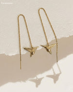 Gold bird-shaped earrings on a beige background