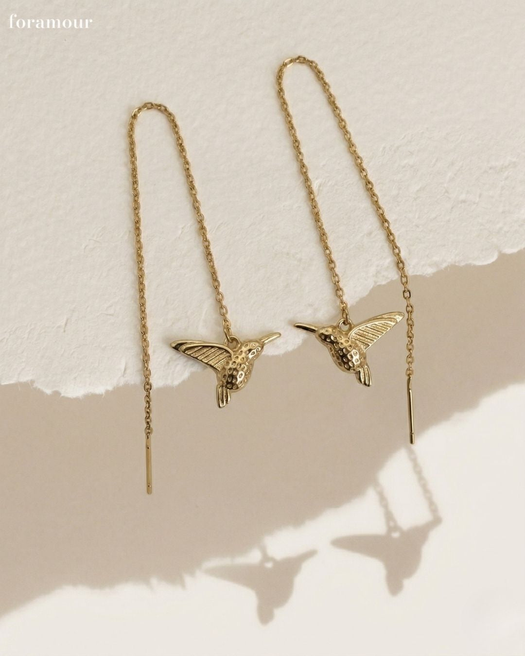 Gold bird-shaped earrings on a beige background