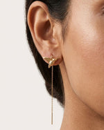 Gold earrings with a bird and chain detail worn by a person 