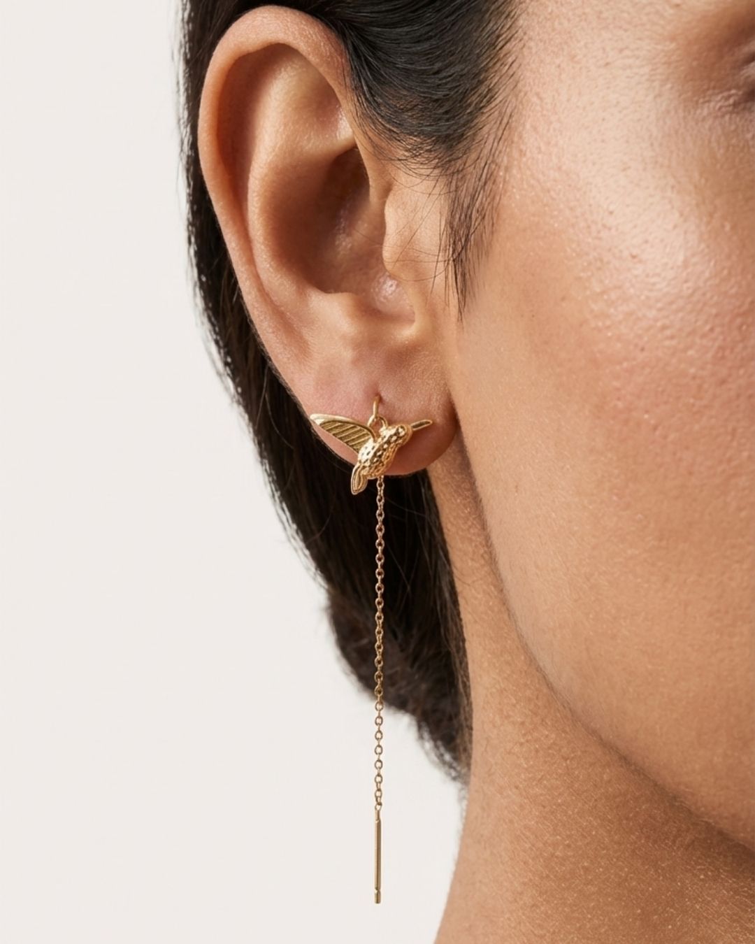 Gold earrings with a bird and chain detail worn by a person 