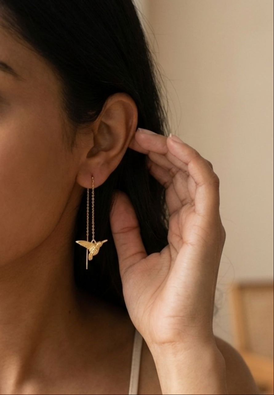Woman wearing a gold bird-shaped earring with a neutral background