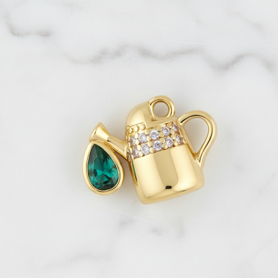Gold charm with green gemstone and diamond-studded band on a white marble background