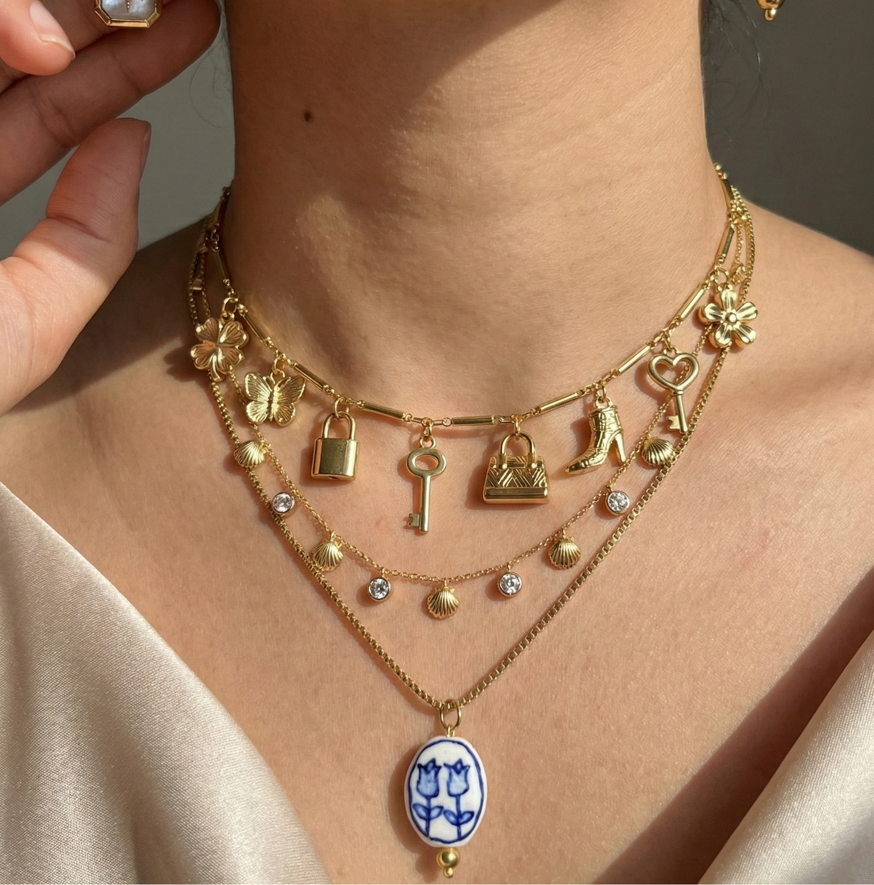 Close-up of a person wearing a gold necklace with various charms and an earring.