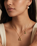 Close-up of a woman wearing a gold necklace with a pendant and pearl earrings.