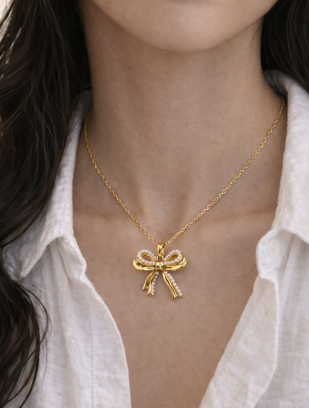 Gold bow-shaped necklace worn by a person with a white shirt.