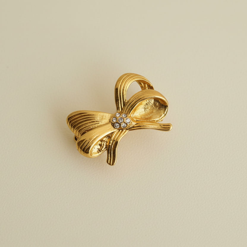 Gold bow-shaped ring on a beige cylindrical object with a light background