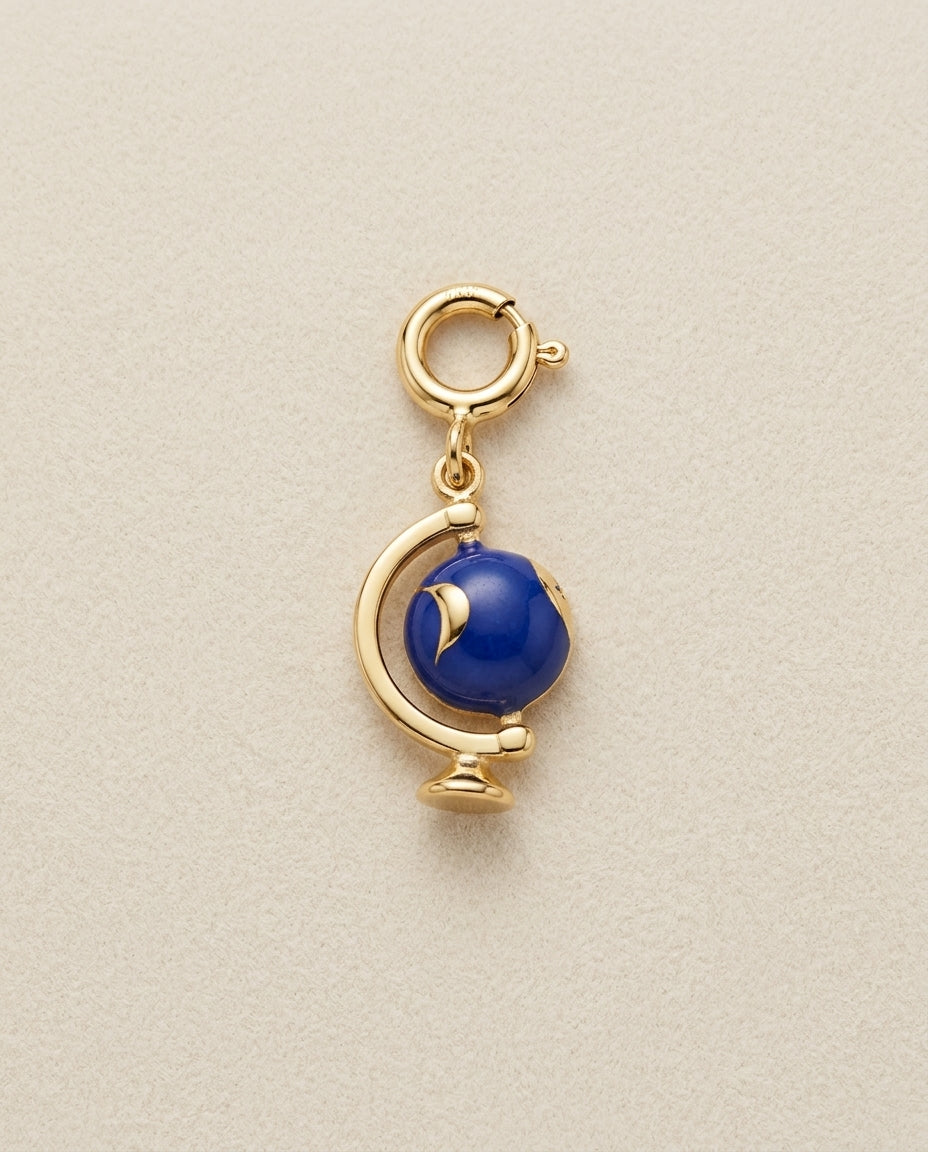 Gold globe charm with a blue gemstone on a beige background
