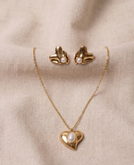 Gold heart-shaped necklace and earrings with pearl accents on a beige fabric background
