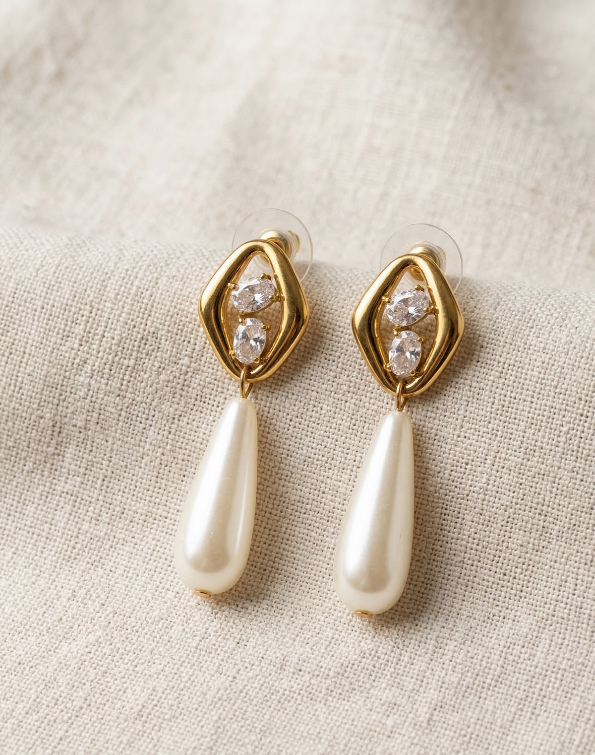 Gold earrings with pearl drops on a beige fabric background