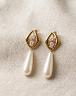 Gold earrings with pearl drops on a beige fabric background