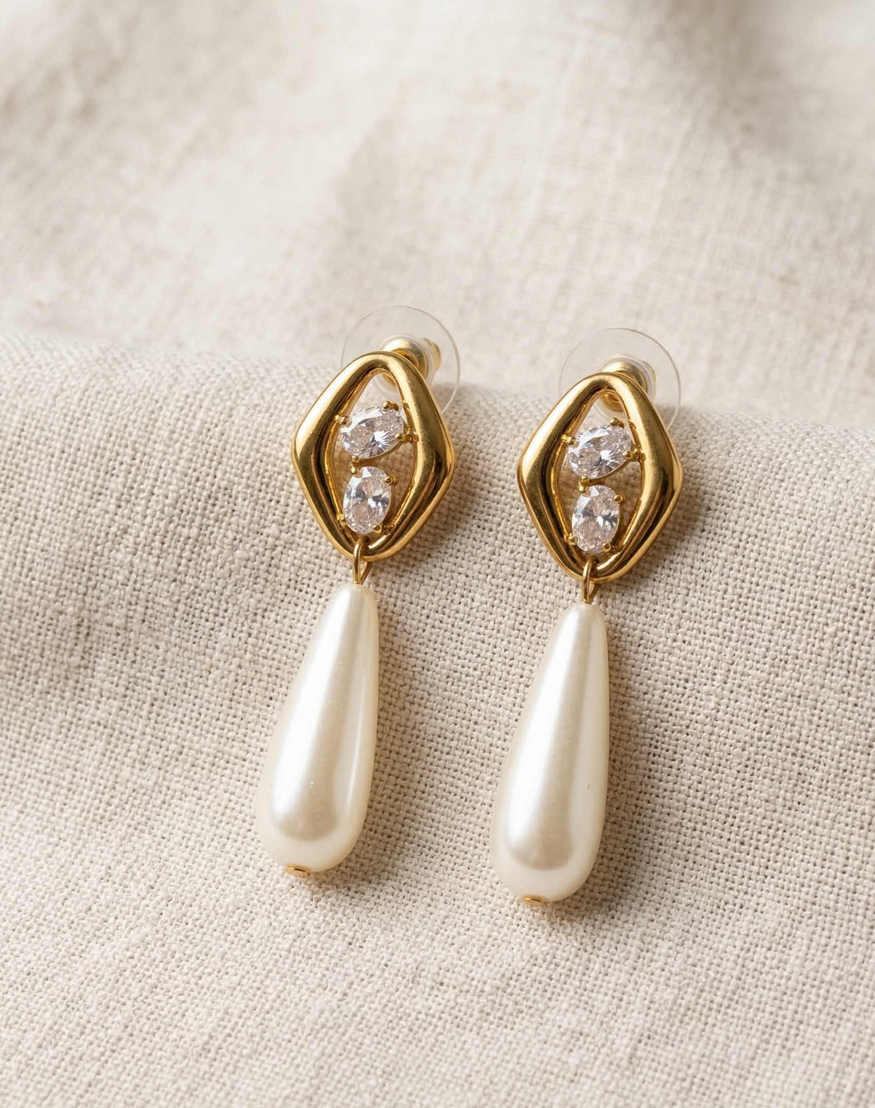 Gold earrings with pearl drops on a beige fabric background