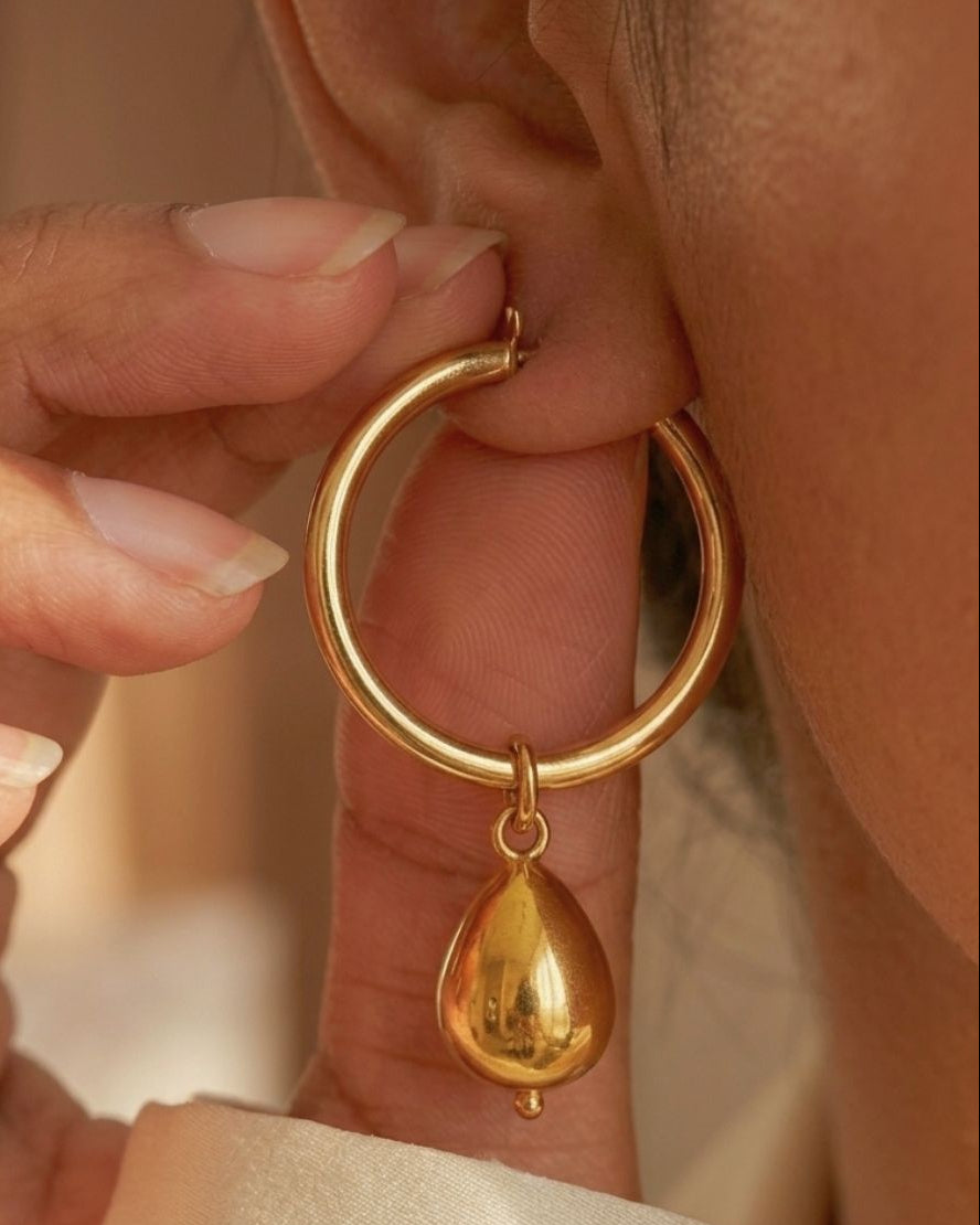 Gold hoop earring with a teardrop pendant being worn.