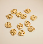 Gold zodiac charm pendants on a textured white background