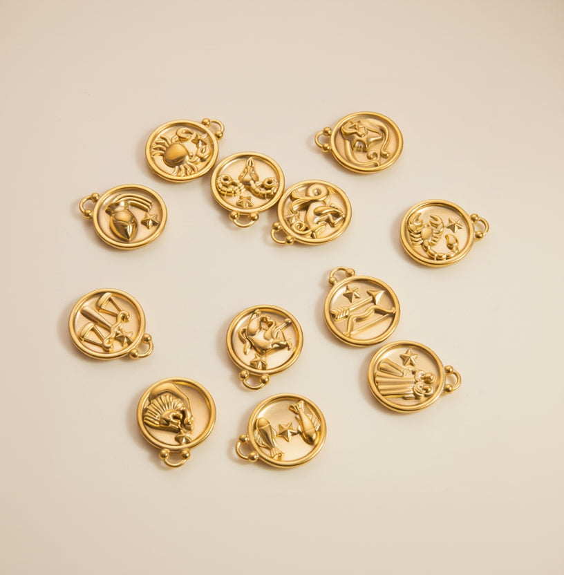 Gold zodiac charm pendants on a textured white background