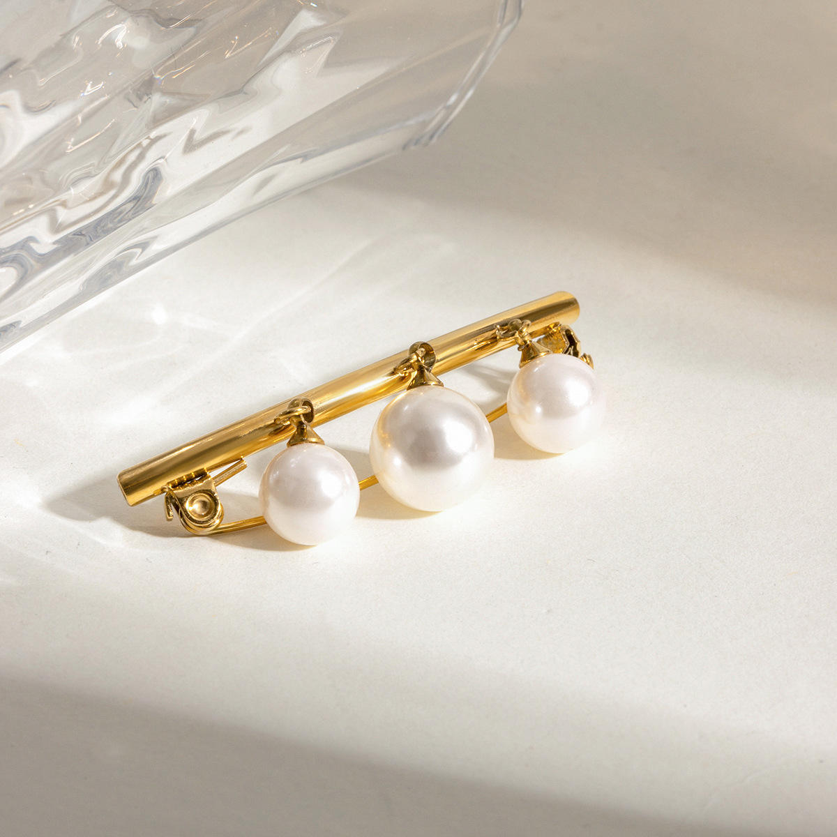 Gold brooch with three pearls on a light background