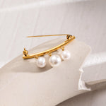 Gold brooch with three pearls on a light background