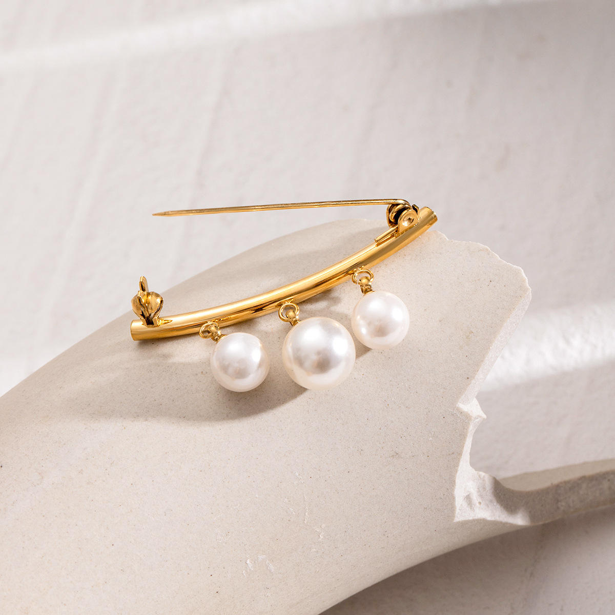 Gold brooch with three pearls on a light background