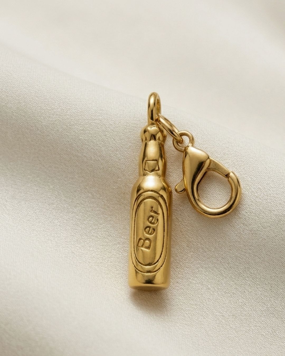 Gold bottle-shaped charm with 'Beer' engraving on a beige fabric background