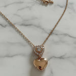 Rose gold heart-shaped necklace with a small heart pendant on a marble background