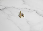 Gold pendant with a blue eye design on a marble surface