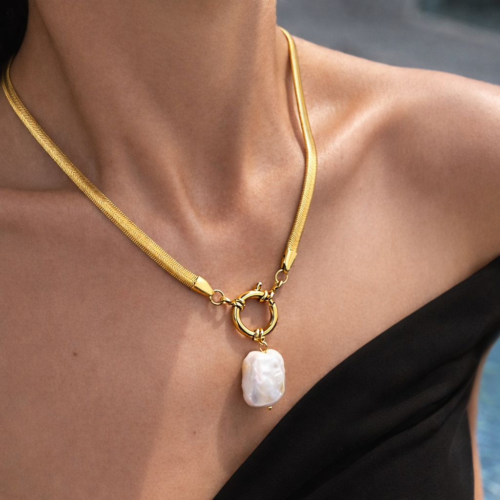 Gold necklace with a pearl pendant on a person wearing a black top.