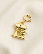 Gold charm shaped like a mixer on a beige background