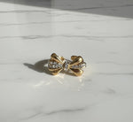 Gold bow-shaped earring with embedded stones on a marble surface