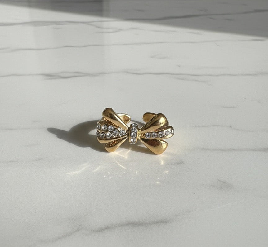 Gold bow-shaped earring with embedded stones on a marble surface