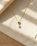 Necklace with green gemstone and pearl pendant on a textured fabric surface