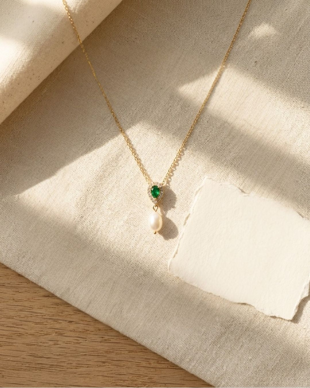 Necklace with green gemstone and pearl pendant on a textured fabric surface