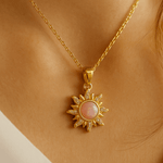 Gold necklace with a sun-shaped pendant featuring a pink stone on a person's neck.