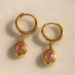 Gold hoop earrings with pink gemstones on a beige background