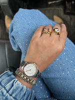Hand wearing a gold watch and rings on a blue textured fabric background