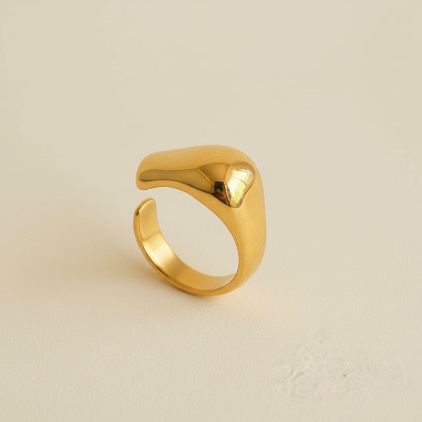 Gold ring on a light gray surface with a beige jewelry box in the background