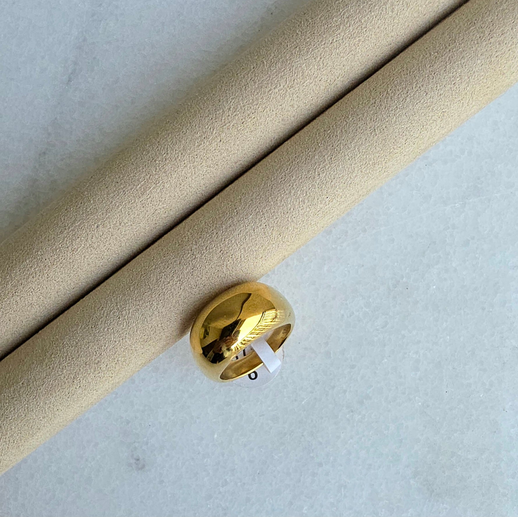 Gold ring on a cylindrical beige object with a light gray background