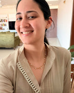 Woman wearing a beige blouse with a white strap over her shoulder in an indoor setting.
